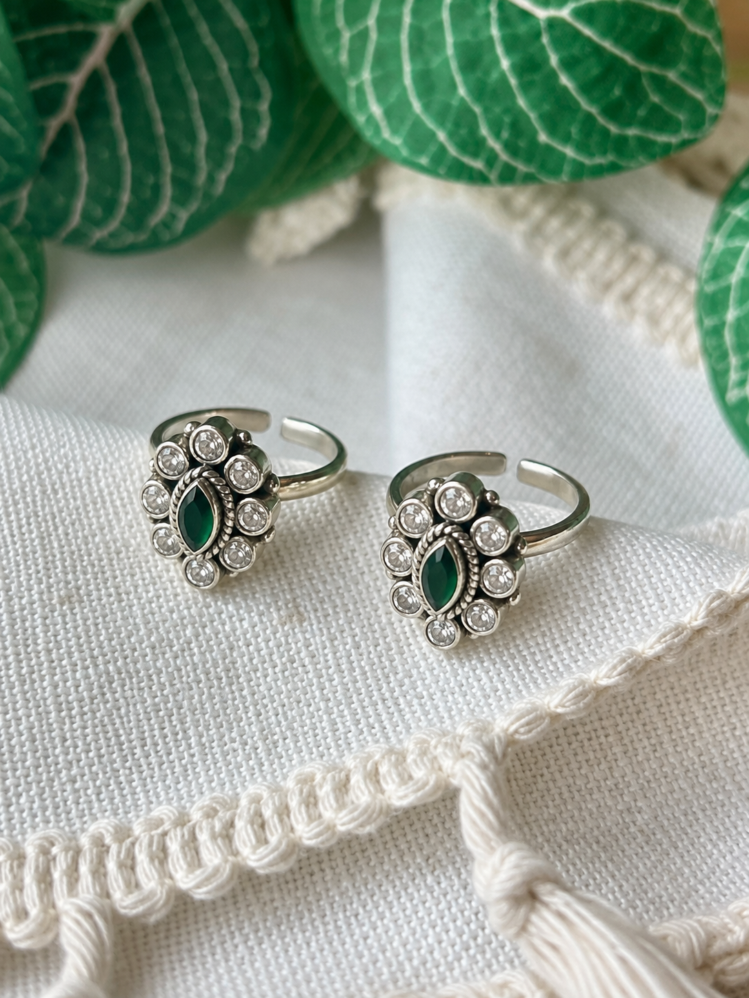     925 silver oxidized halo toe ring pair with green centre stone displayed on white linen fabric