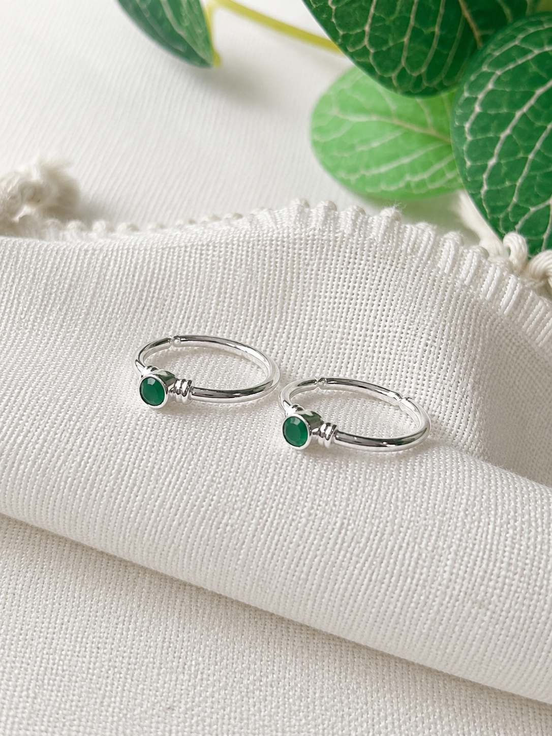  925 silver minimal toe ring pair with small round green stones on white fabric