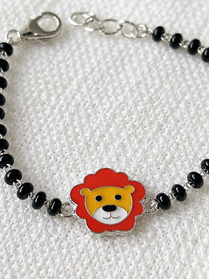 A silver beaded bracelet with a central lion head charm featuring a red mane, yellow face, and white details, displayed on a textured white fabric background.