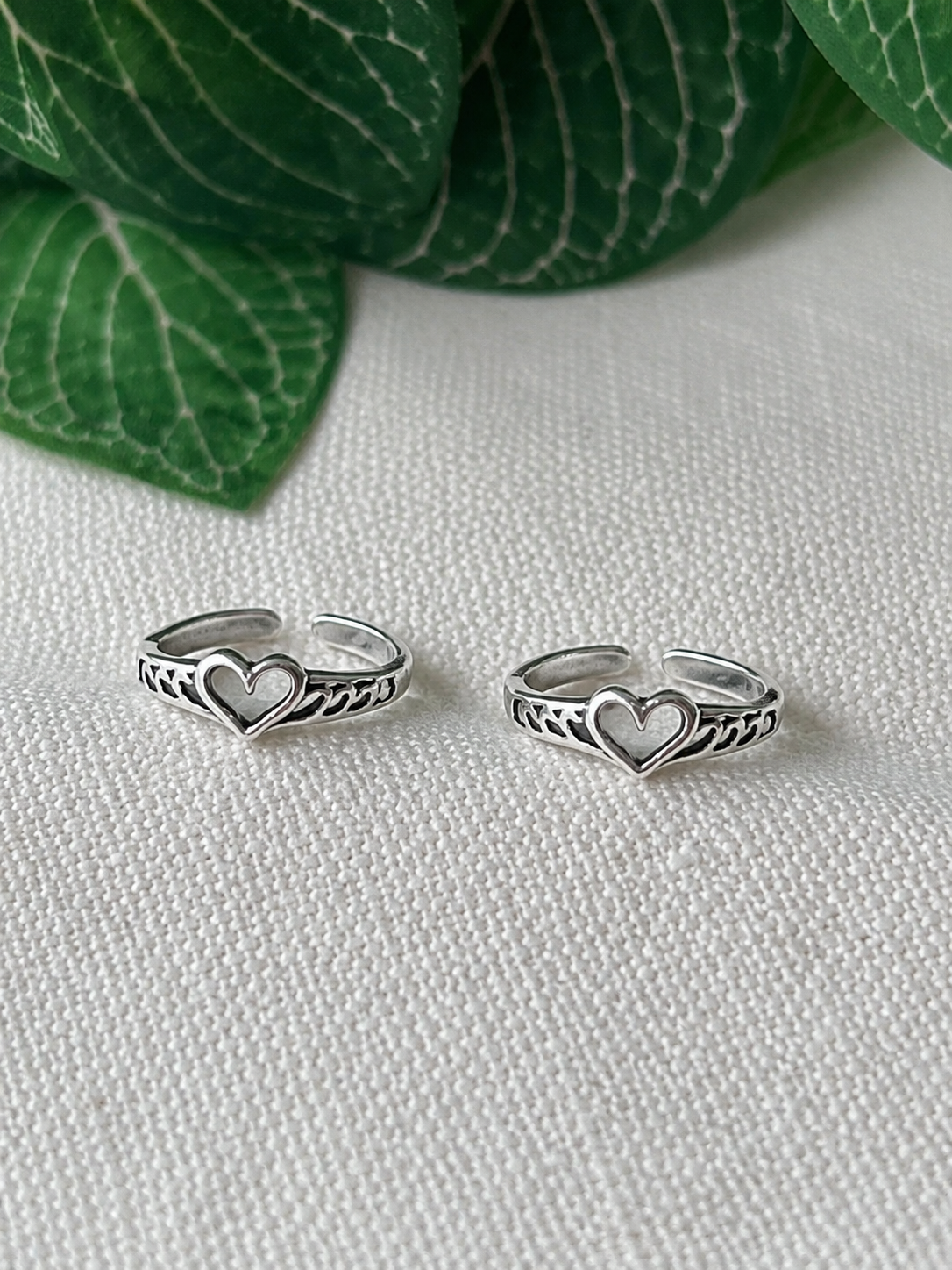925 silver heart motif toe ring pair on linen fabric with leaves