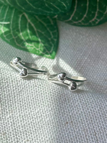 A pair of silver-toned bone-shaped rings displayed on a textured white fabric surface with green leaves in the background.