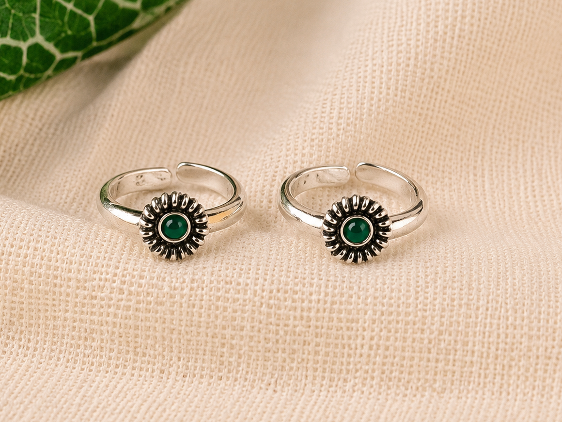 925 silver sunburst toe ring pair with green stone on linen fabric